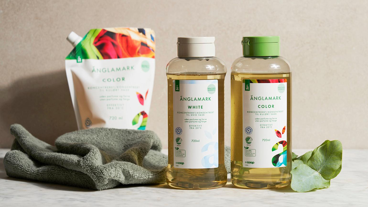 Änglamark White tøyvask og Änglamark Color tøyvask på marmorbord, med grønt håndkle og eucalyptusblad på siden. Änglamark Color refill i bakgrunnen.