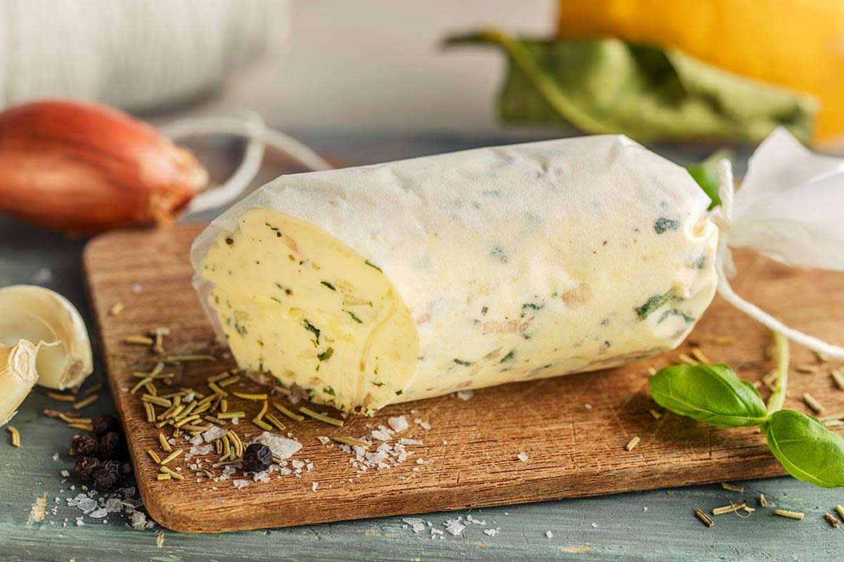 Kryddersmør med hvitløk, basilikum, sjalottløk og sitron pakket i matpapir og rullet til en pølse. Servert på liten trefjøl med ferske urter og krydder rundt.