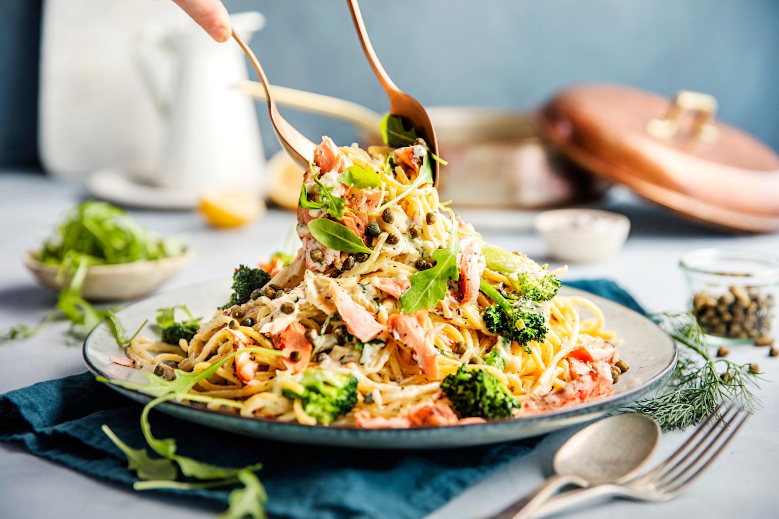 Pasta med laks og kapers. Noen forsyner seg med bestikk.