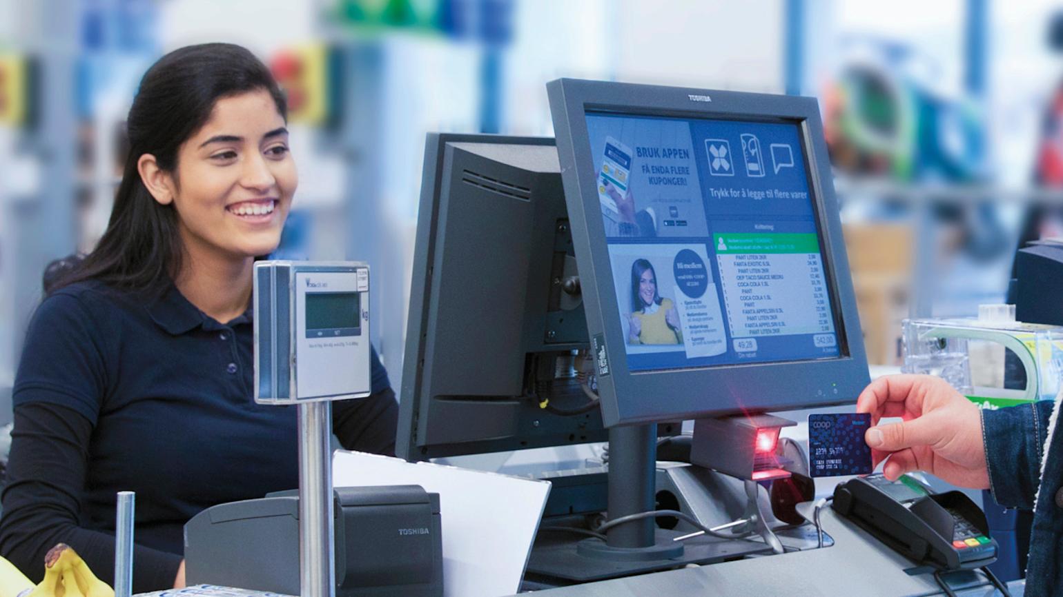 Dame med mørkt hår smiler og sitter i butikkassen