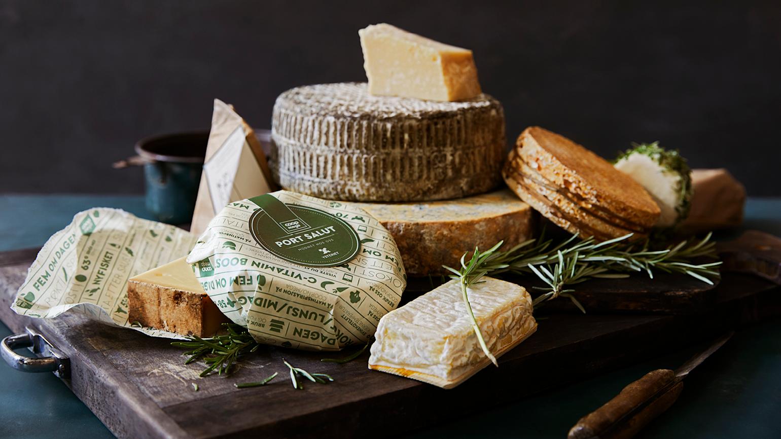 En trefjøl med ulike oster og rosmarinkvister på, med mørk bakgrunn.