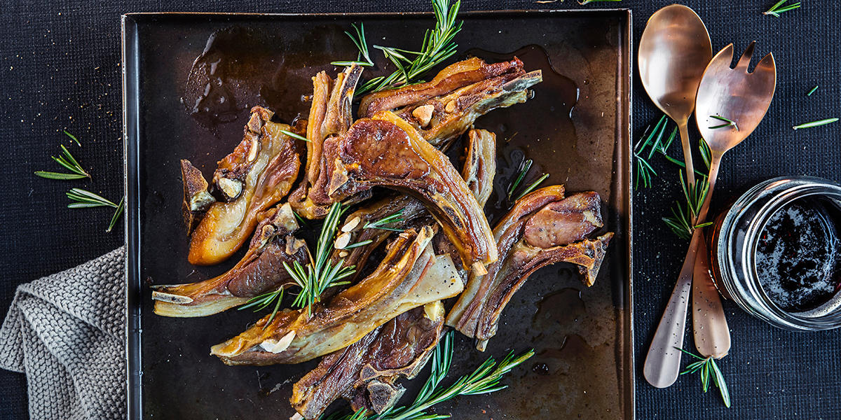 Fat med dampet pinnekjøtt på kryss og tvers, med frisk rosmarin på toppen. Mørk bakgrunn.