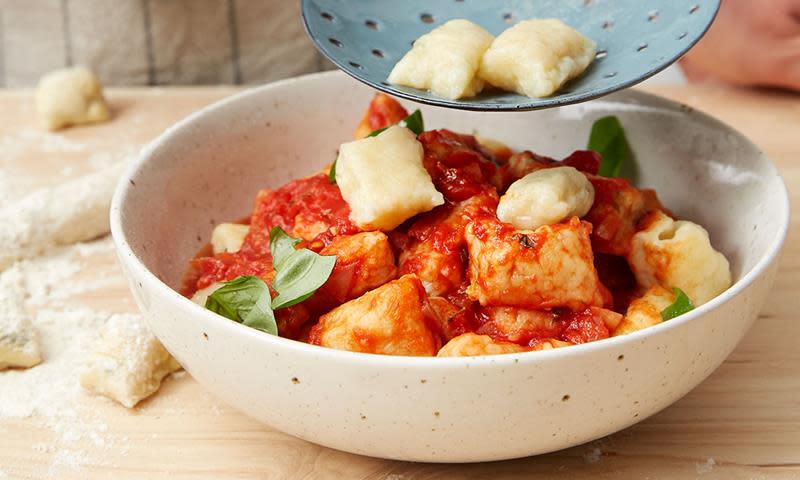 Billig gnocchi med tomatsaus. Hjemmelaget gnocchi av potet, med hjemmelaget tomasaus, servert i lys pastabolle med fersk basilikum, på lys trebakgrunn.