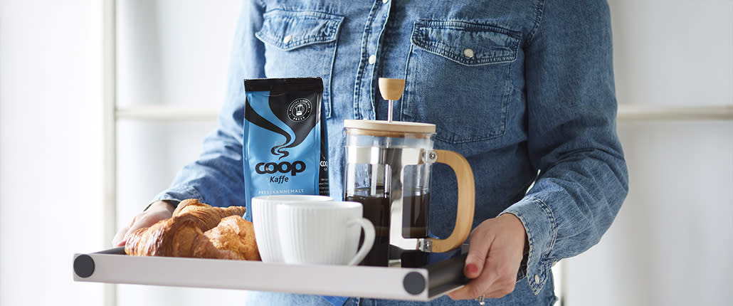 Coop Kaffe - Kvinne bærer brett med bakevarer og blå Coop kaffe