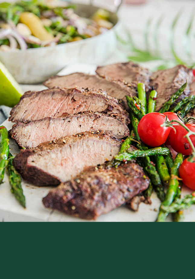 Oppskåret biff på en hvit fjøl med tomater og asperges rundt.
