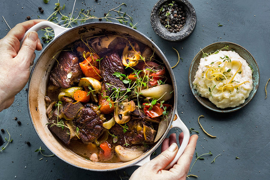 Fransk gryterett med sitronpotetmos, servert i lys jerngryte med rotgrønnsaker, løk og friske urter. Liten skål med sitronpotetmos på siden.