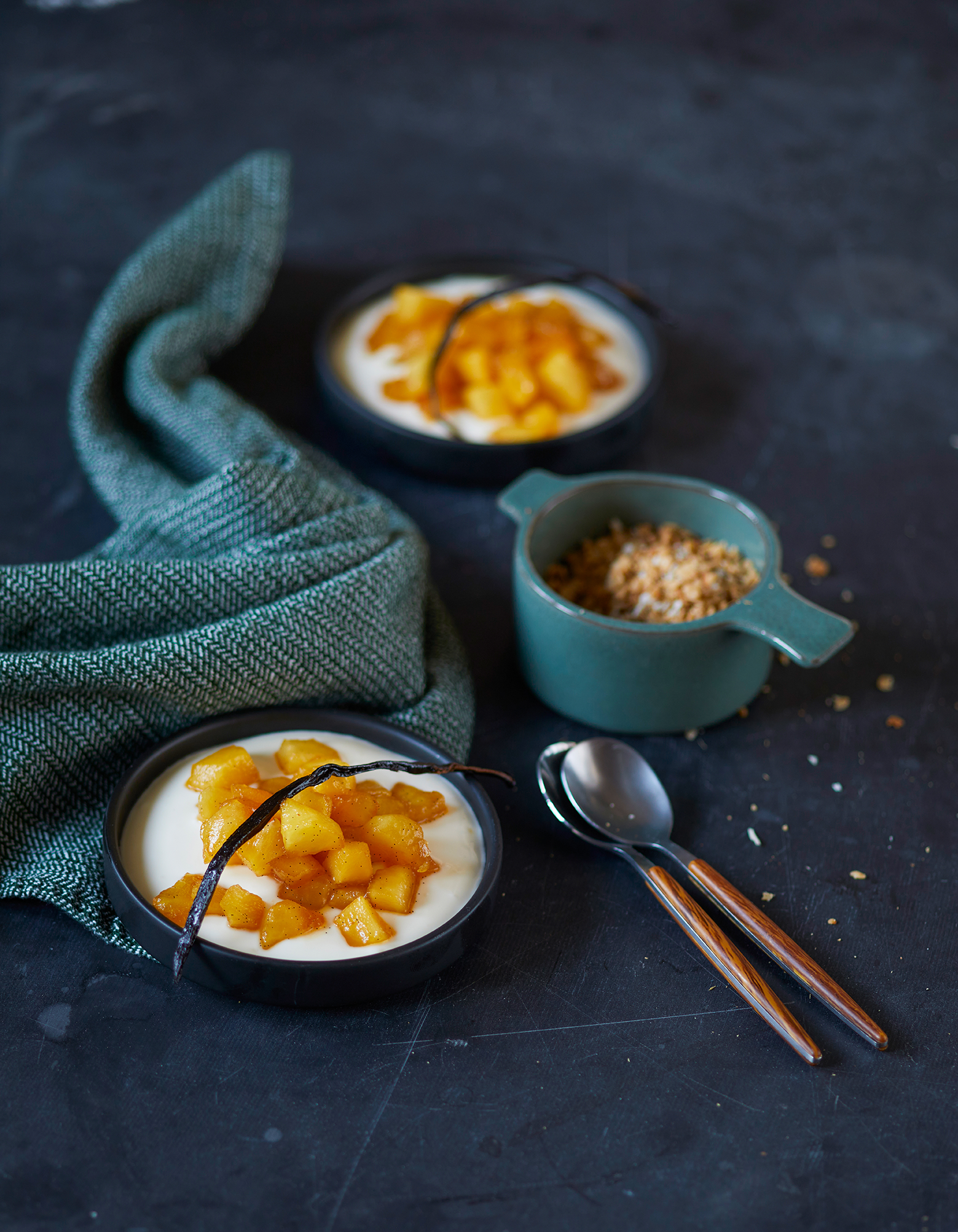 Vaniljebakte epler med mascarpone- og rømmekrem, servert i svarte små skåler, med krokan i blå skål ved siden av.