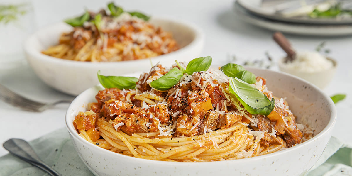 Spagetti bolognese i hvit skål med basilikum og parmesaen