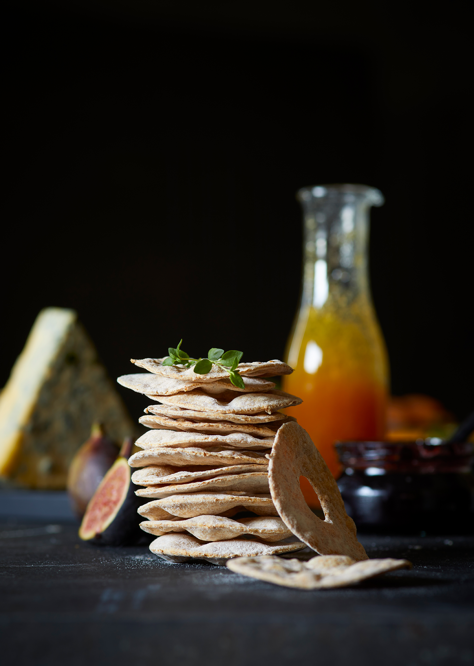 Runde knekkebrød stablet på bord, og servert til blåmuggost, marmelade, ferske fiken og urter.