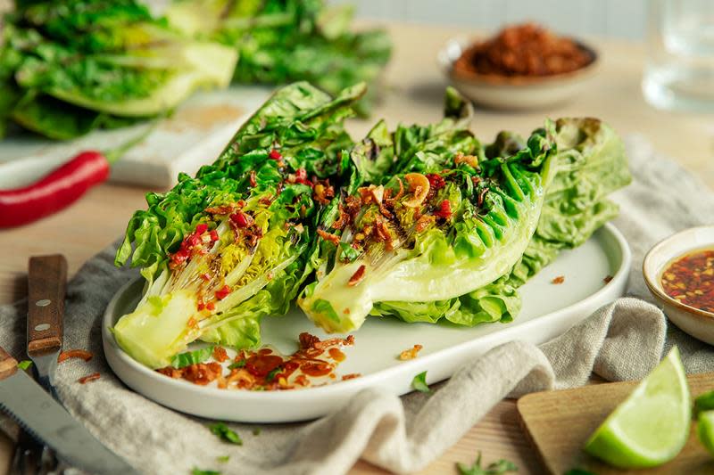 Grillet hjertesalat delt i to, toppet med asiatisk dressing på soya, chili, ingefær og hvitløk. Servert på fat, med limebåter ved siden av.