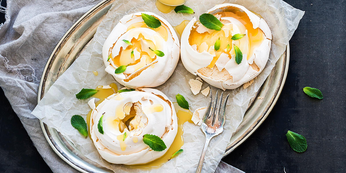 Mini pavlova med lemon curd og mynteblader, på sølvfat på mørk bakgrunn.