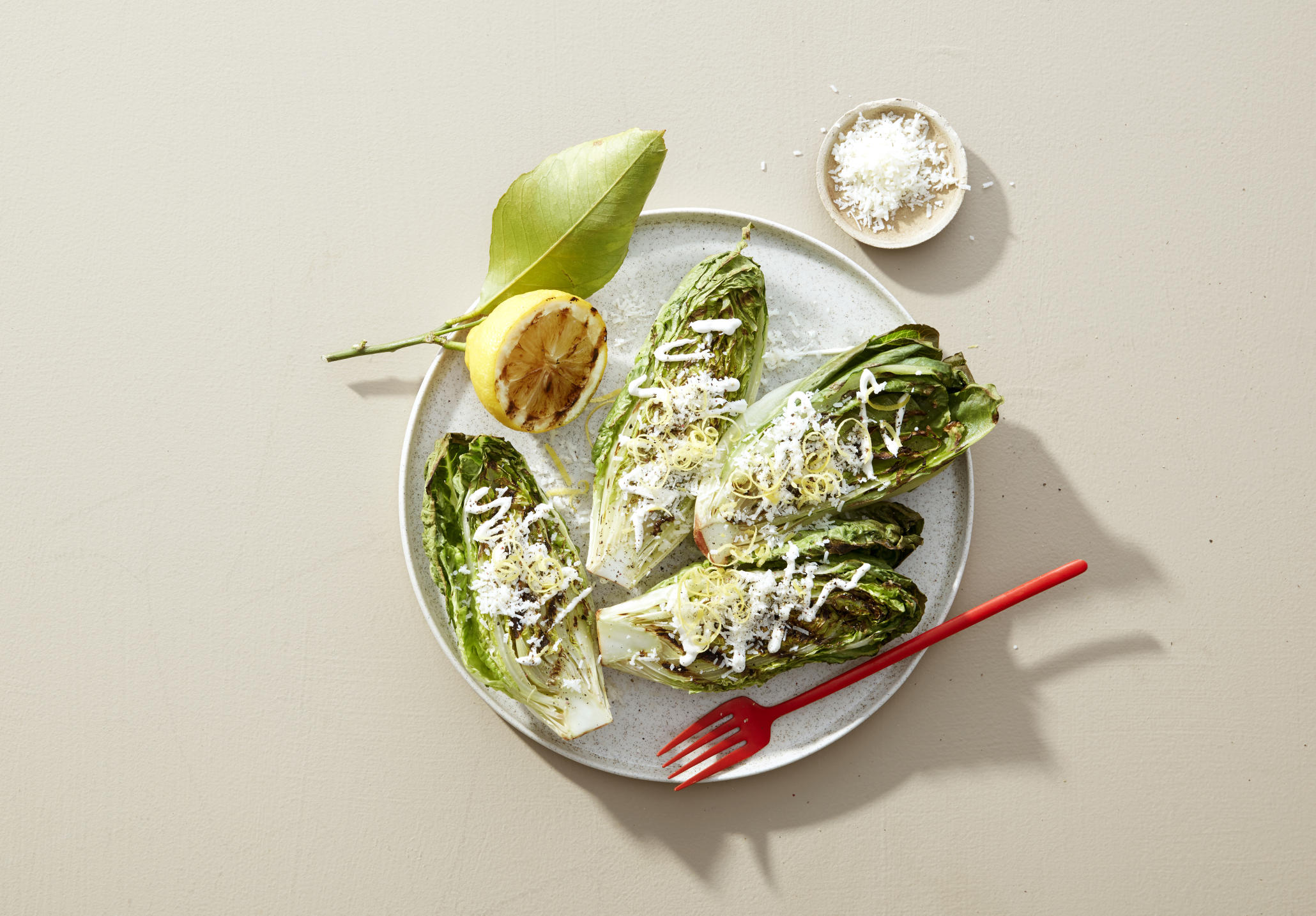 Grillet hjertesalat toppet med dressing, parmesan og sitronskall. Servert på lys tallerken.