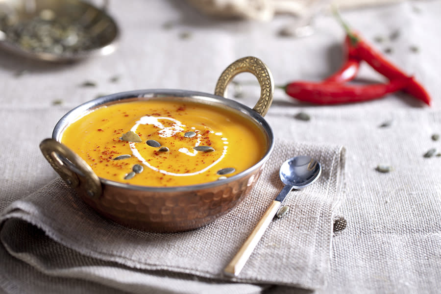 Suppeskål med gresskarsuppe toppet med gresskarkjerner, litt rømme og chilipulver.