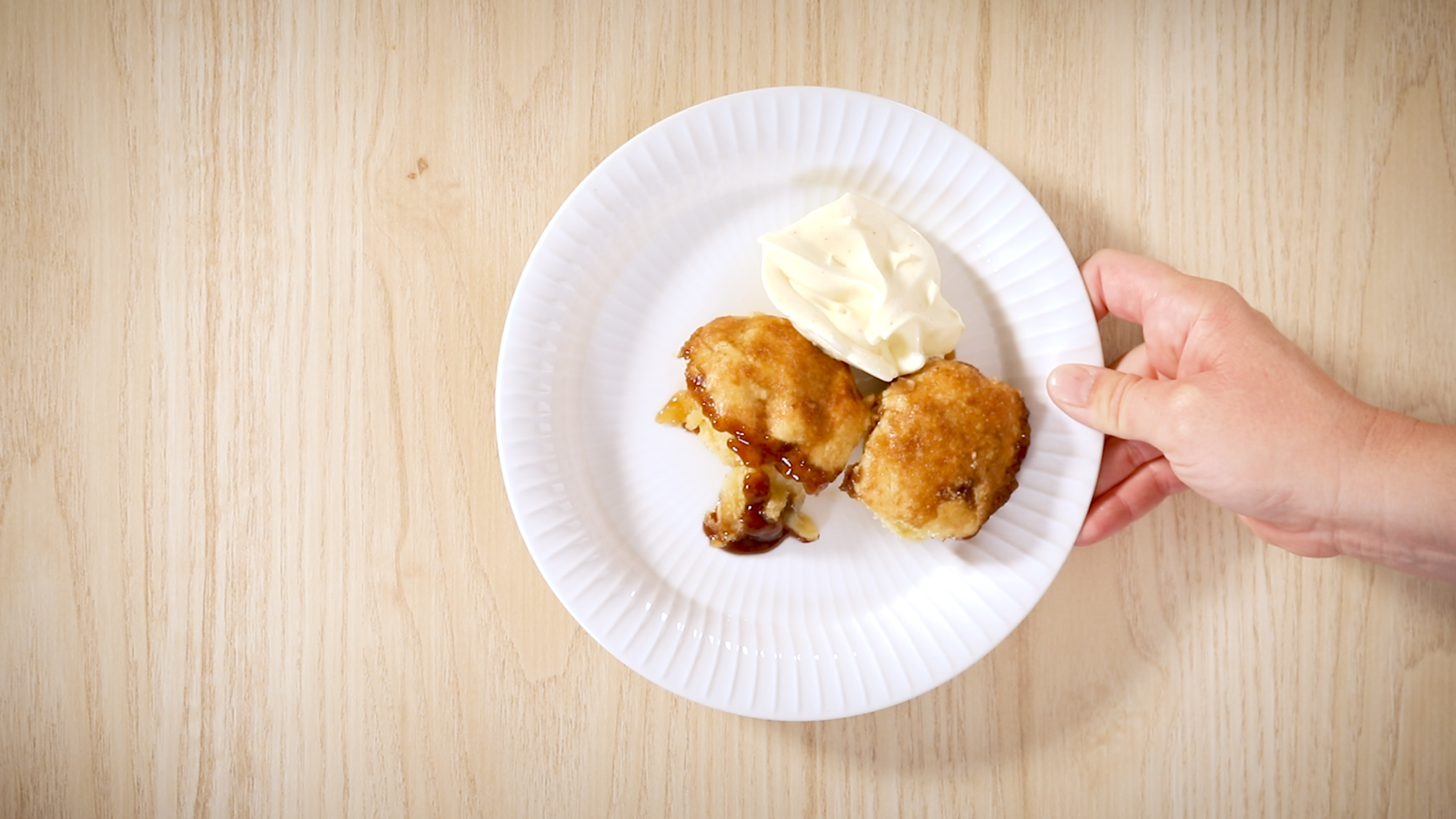 Dumplings med epler, servert på hvit tallerken med vaniljeis. En hånd holder tallerkenen over et lyst trebord.